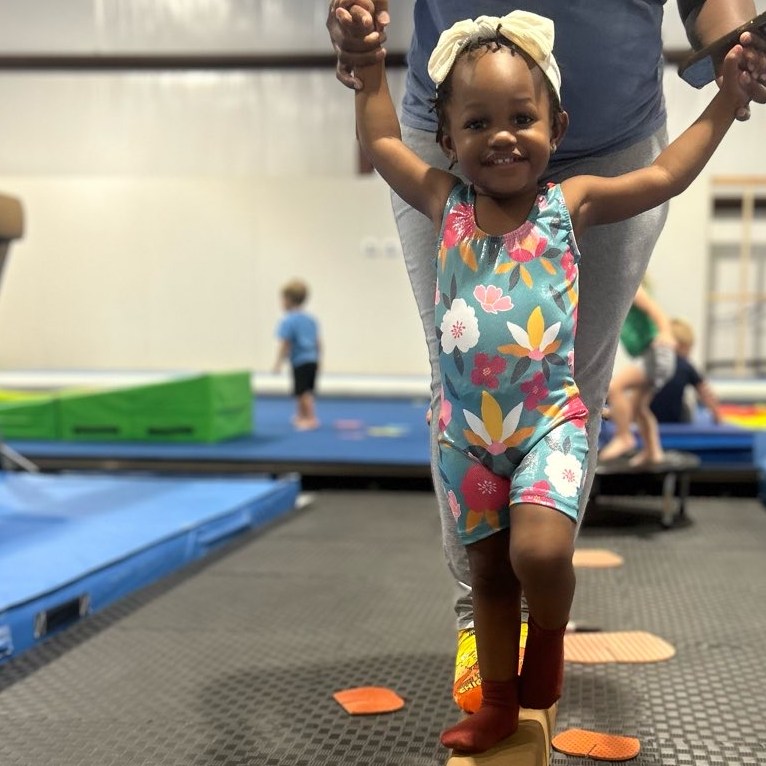 Little girl on balance beam being helped by adult at Riverfront Gymnastics