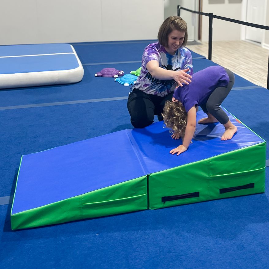 Staff member assisting girl doing forward roll